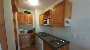 Een kleine keuken met houten kastjes, een magnetron, een fornuis, een spoelbak en een vaatwasser.