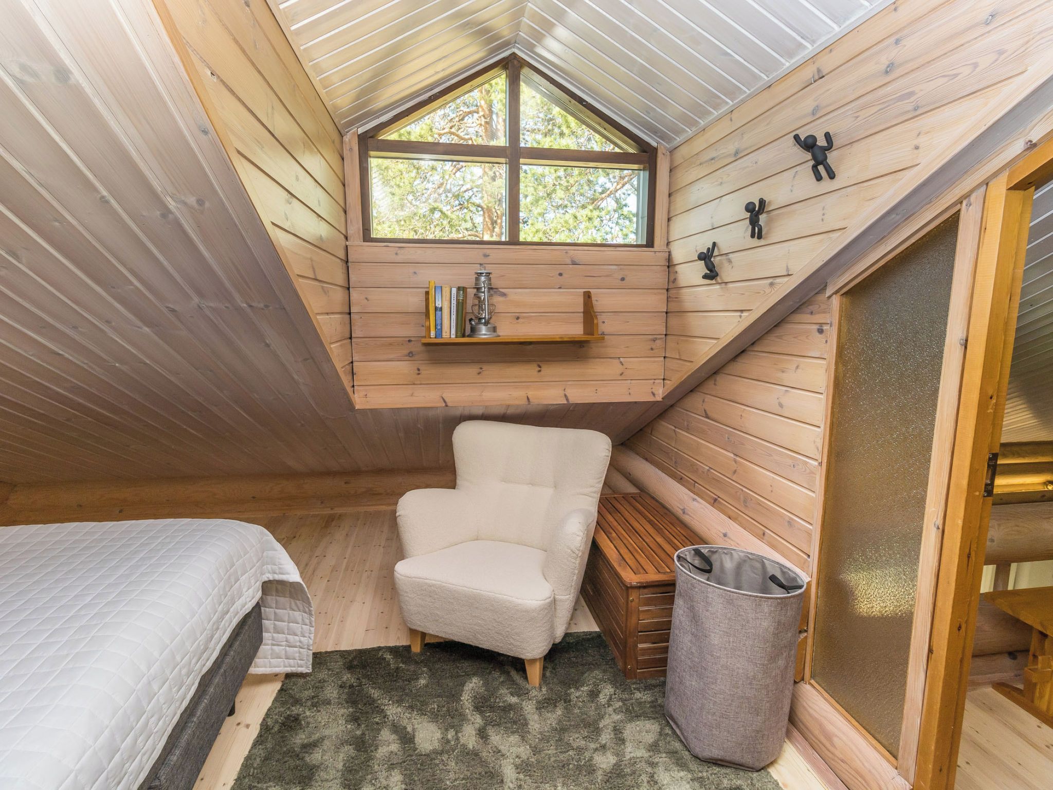 Een gezellig slaapkamer op zolder met een schuine kap, een raam, een boekenplank, een stoel, een bed en een afvalbak.