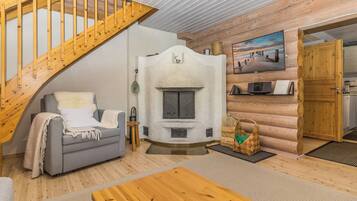 A cozy cabin interior with a wooden staircase, a fireplace, a sofa, and a television.