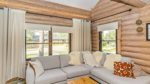 A cozy log cabin interior with a sectional sofa, a wooden coffee table, and large windows offering a view of the outdoors. - Kiilopään tunturimajat b6 / kerttula by Interhome (Inari)