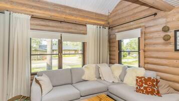 A log cabin interior with a sectional sofa, a wooden coffee table, and large windows.