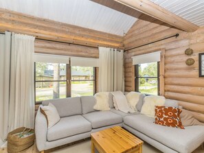 A log cabin interior with a sectional sofa, a wooden coffee table, and large windows.