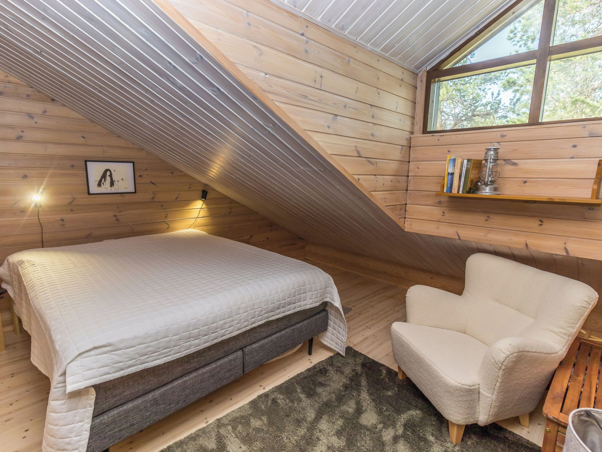 Een slaapkamer met een bed, een stoel, een plank met boeken en een ingelijst schilderij aan de muur.