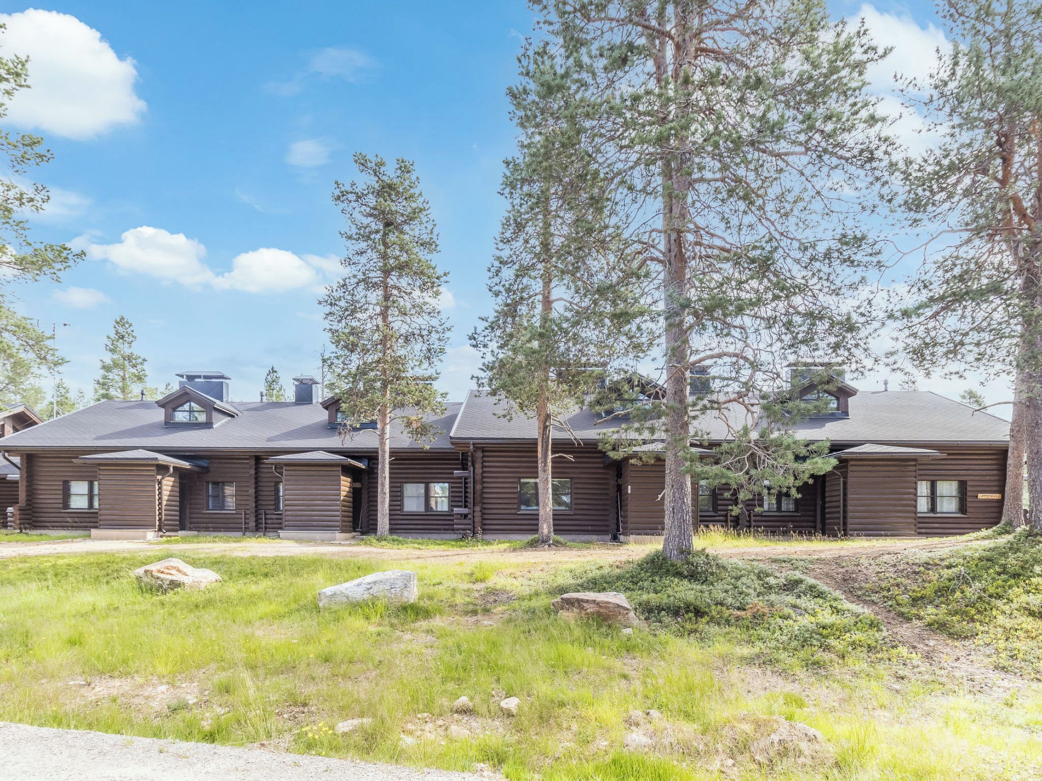 Une rangée de bâtiments construits dans le style des cabanes en rondins, avec un pré verdoyant au premier plan et des arbres.
