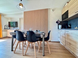 A modern kitchen with wooden cabinets, a built-in microwave, and a dining area with a table and chairs. - Cozy apartment at the foot of the slopes with pool (Flumet)