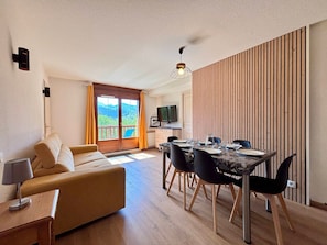 A modern living room with a sofa, dining table, and chairs, a TV, and a view of the outdoors.