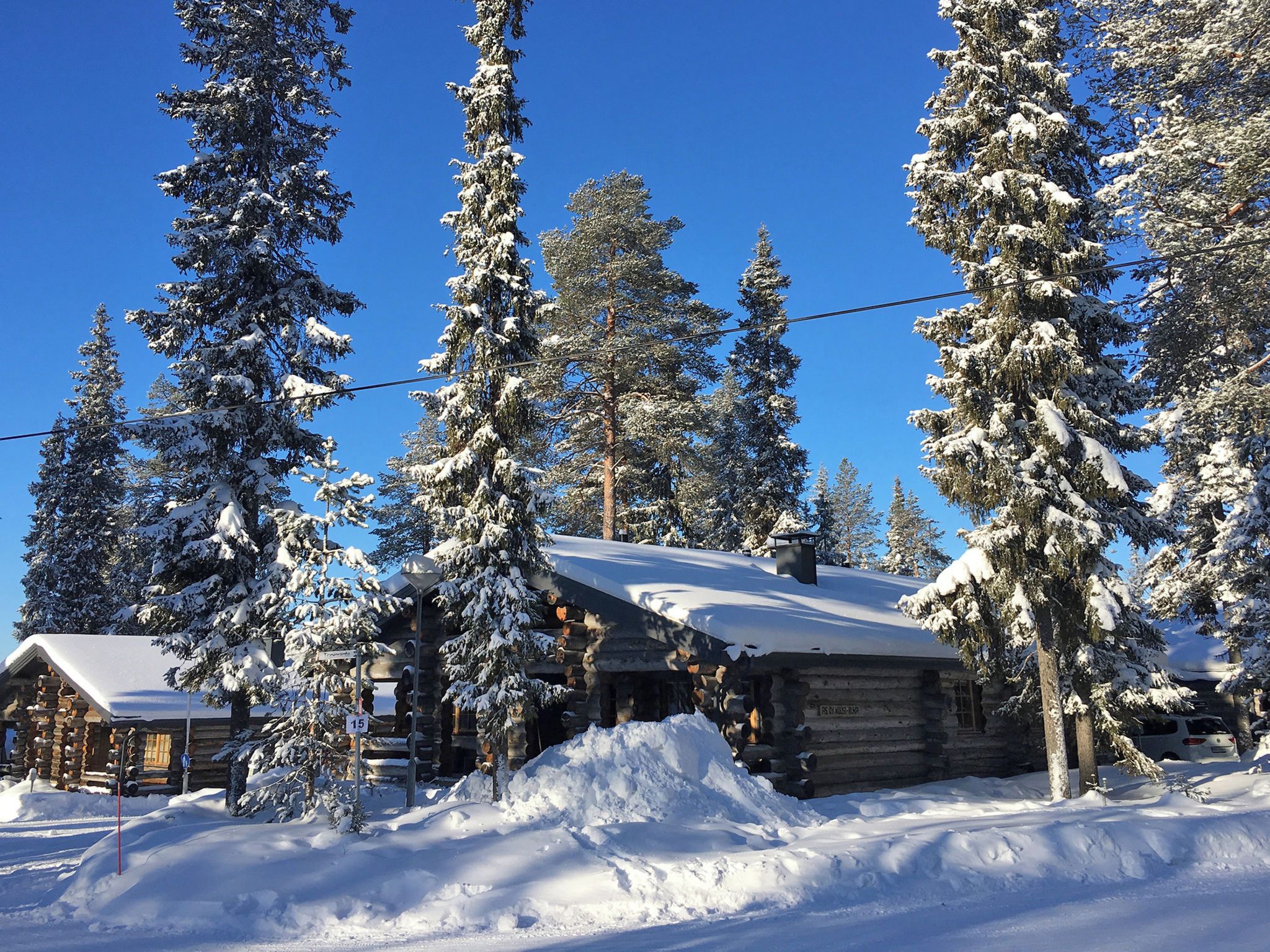 A log cabin surrounded by snow-covered trees, with a clear blue sky above.