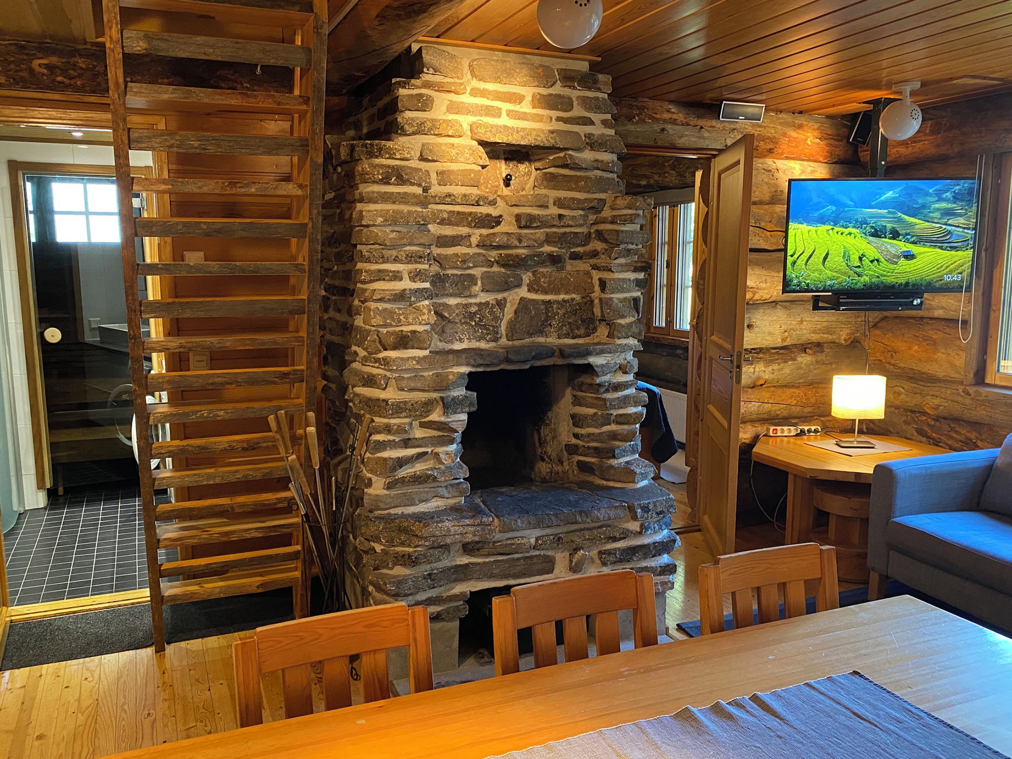 A rustic interior with a stone fireplace, wooden furniture, and a television mounted on the wall.