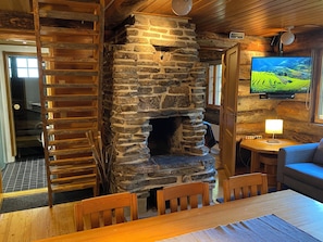 A rustic interior with a stone fireplace, wooden furniture, and a television mounted on the wall.