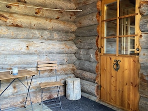 A rustic log cabin interior with a wooden door, a bench, a table, and a small stool.