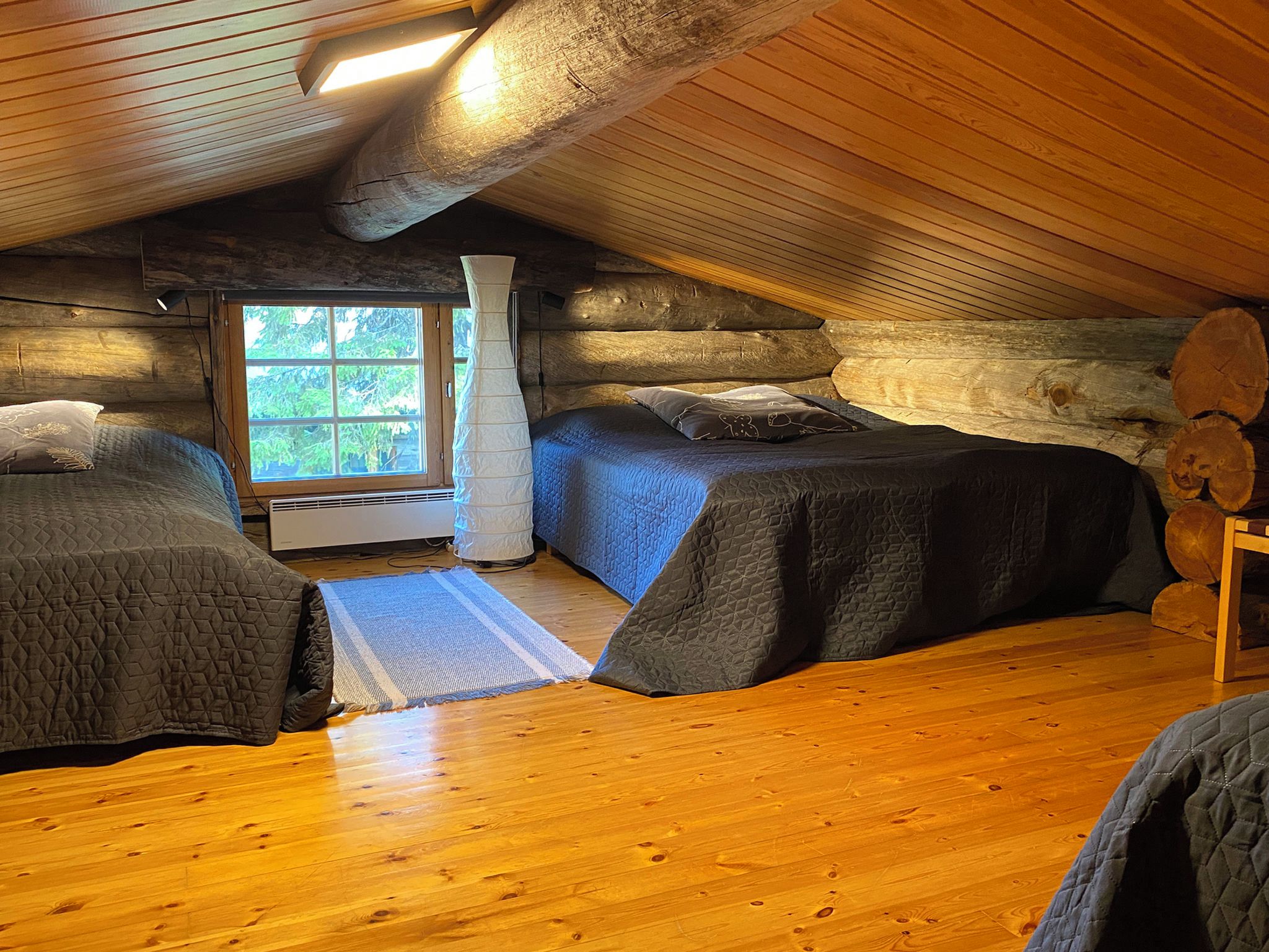A cabin with two beds, wooden walls, a window, and a wooden floor.