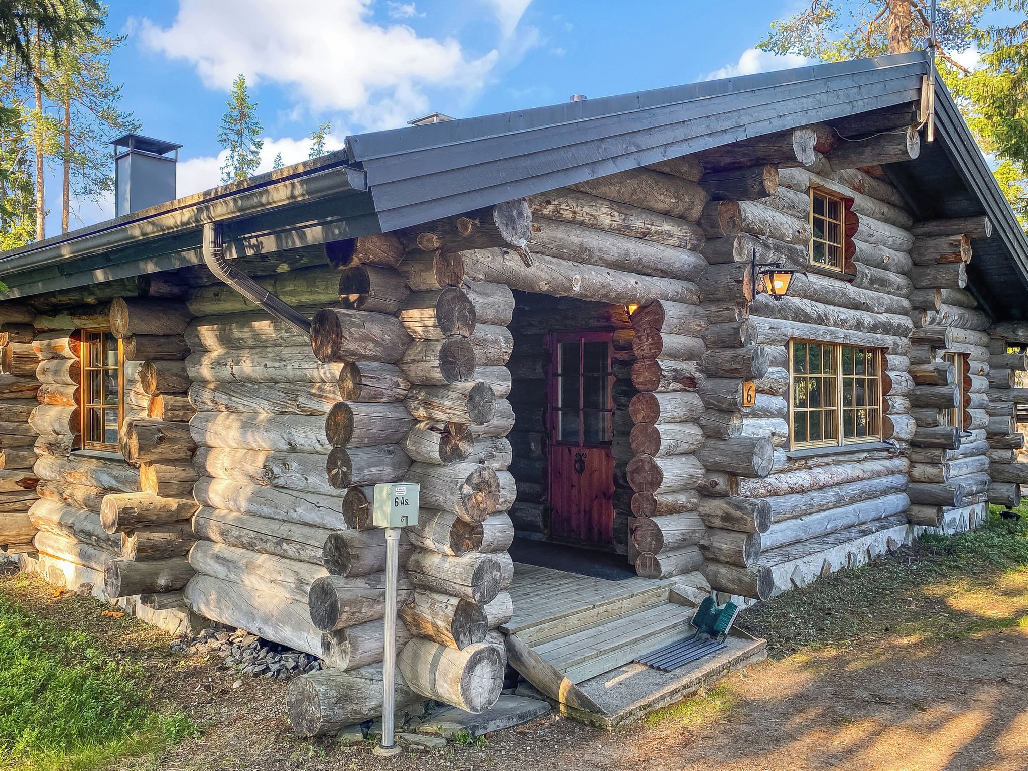 A log cabin with a wooden porch, a red door, and a small window.