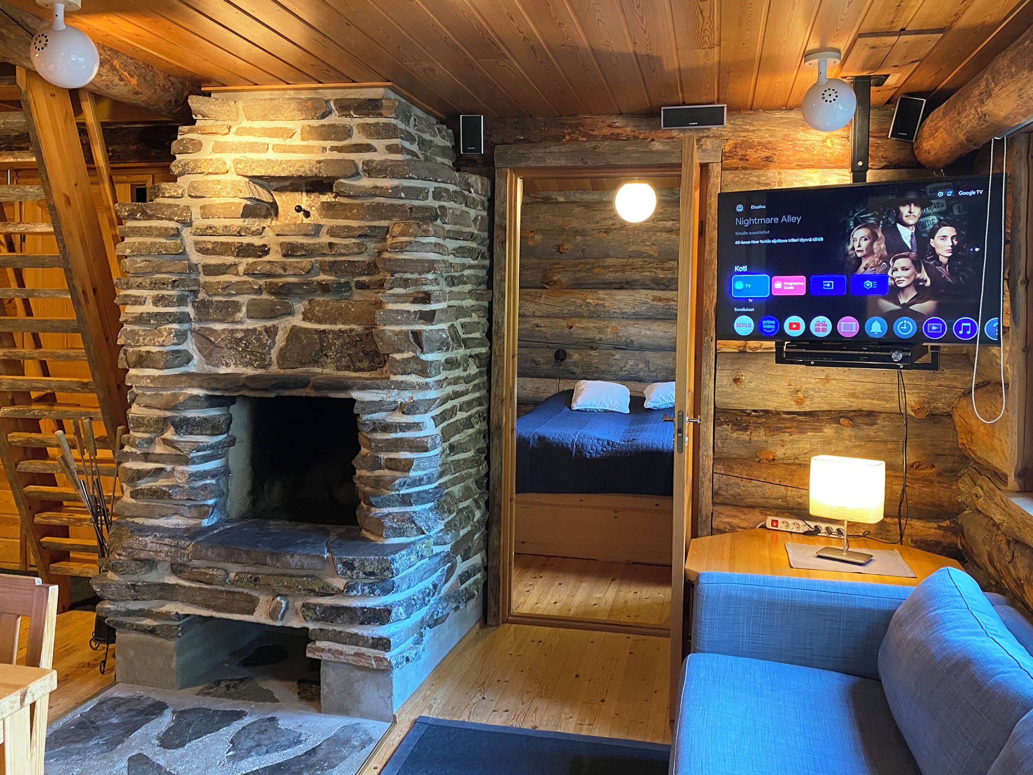 Una habitación acogedora con chimenea de piedra, televisor montado en la pared y techo de madera.
