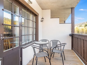 Une terrasse en bois avec une table et des chaises, une porte dotée de grandes fenêtres et une vue sur une zone boisée.