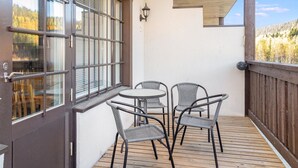 Een balkon met een houten terras, een tafel en vier stoelen.