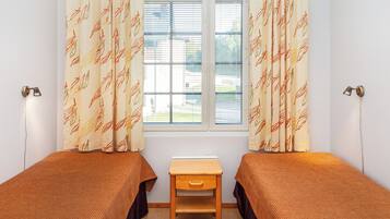 A room with two single beds, a small wooden nightstand, and a window with blinds.