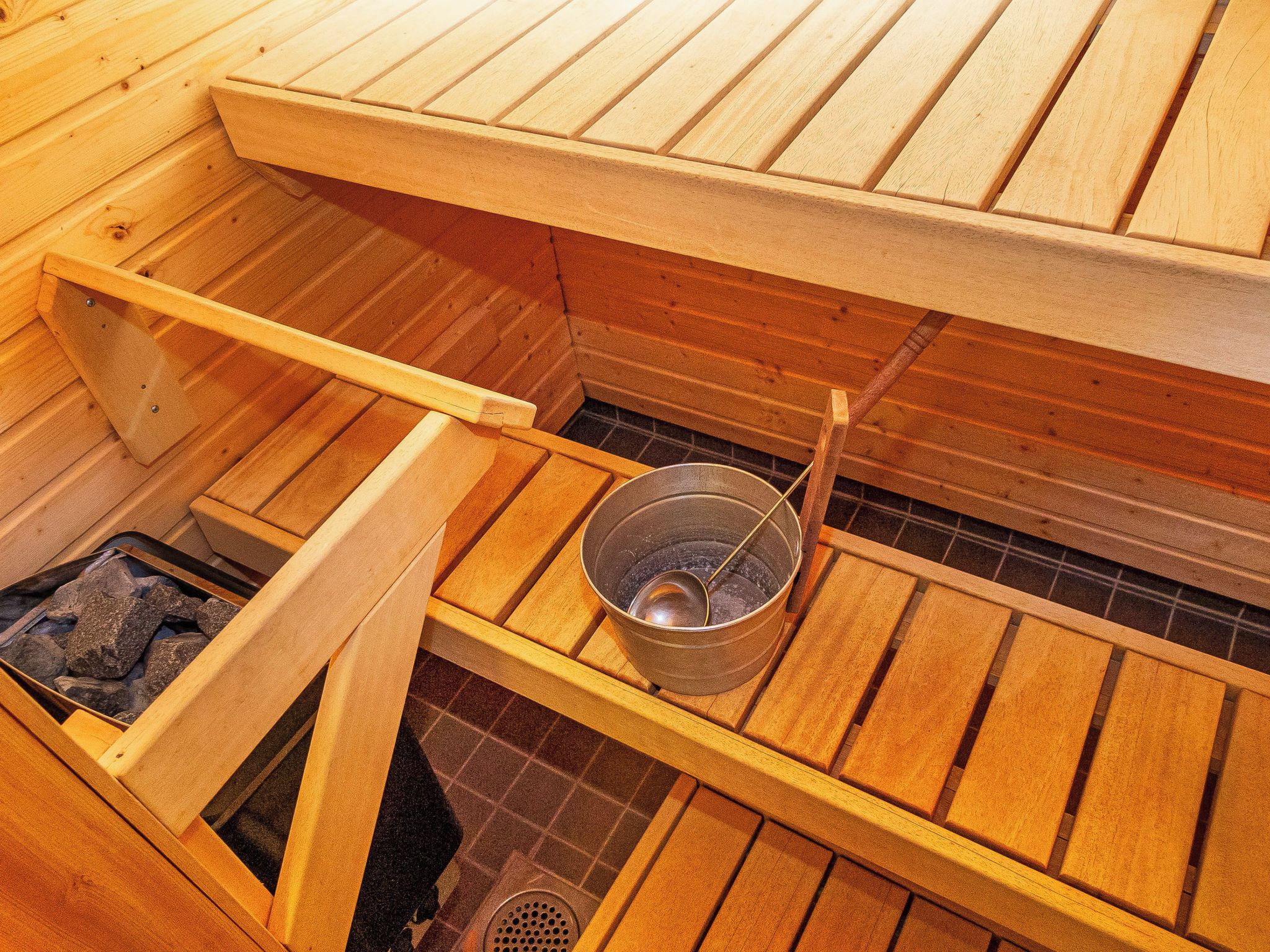 Un sauna avec des bancs en bois, un seau en métal et une grille pour brûler du bois.