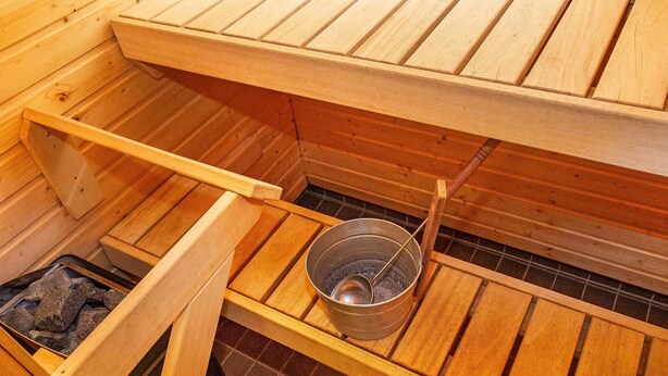 Een sauna met houten banken, een metalen emmer en een rooster voor het branden van hout.