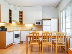Een compacte keuken met witte kasten, een magnetron, een fornuis en een eethoek met houten stoelen en een tafel.
