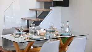 A modern dining area with a glass table, wooden chairs, and a staircase with built-in shelves.