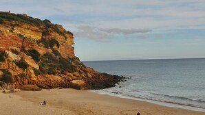 A beach with a rocky cliff, calm sea, and a few people.