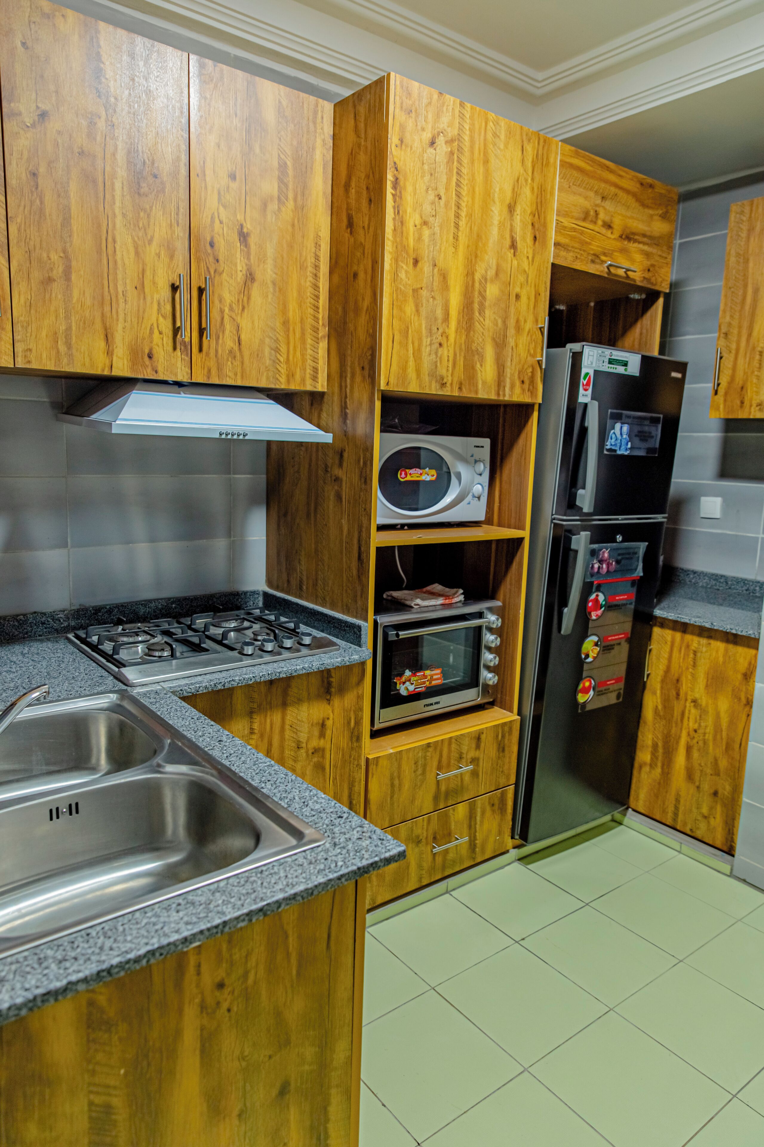 Una cuina amb armaris de fusta, fogó a gas, microones, forn integrat i nevera.
