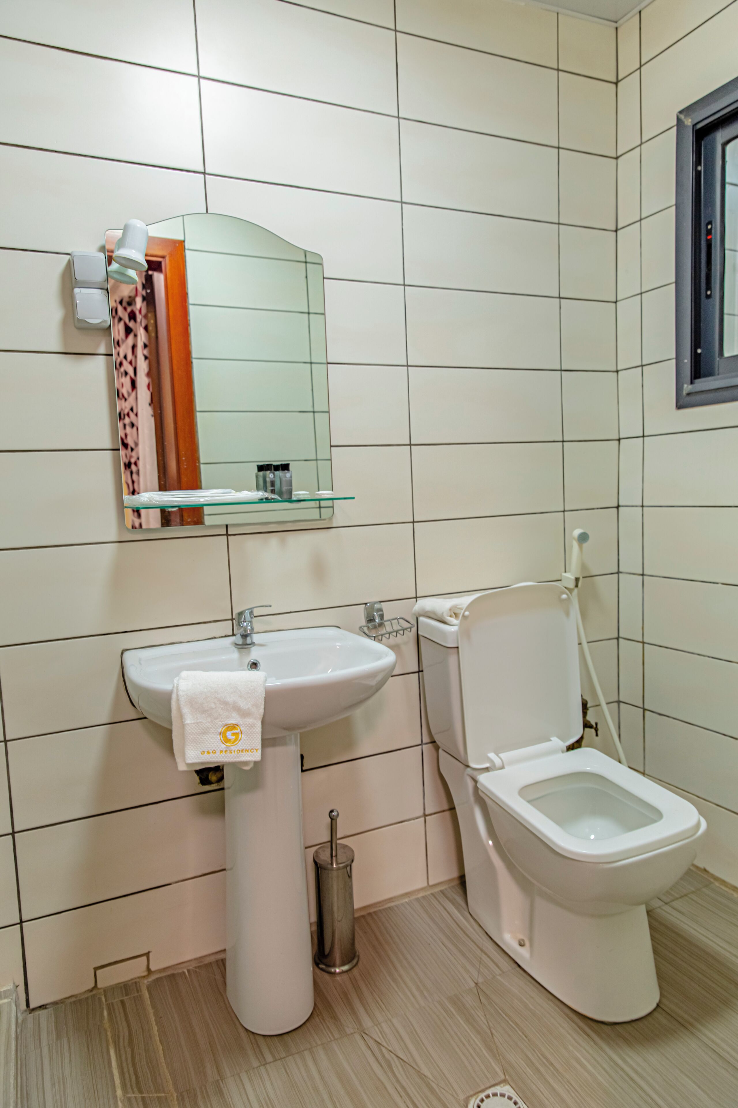 Et badeværelse med håndvask, toilet og et spejl over håndvasken.