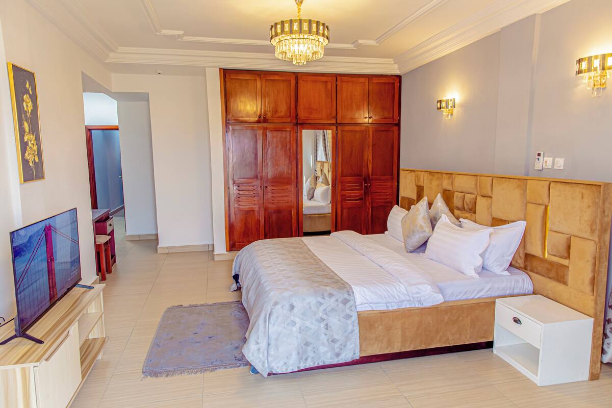 Quarto com cama grande, televisão, guarda-roupa de madeira e um candelabro.
