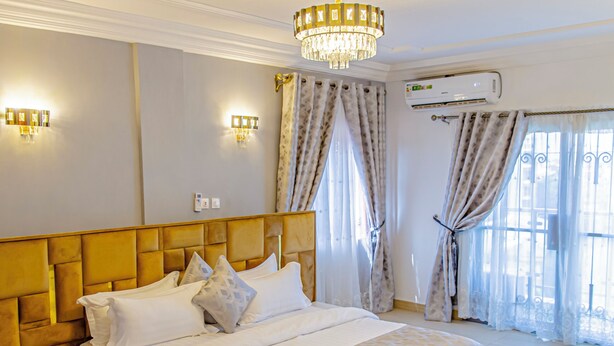 A bedroom with a large bed, a nightstand, a chandelier, and an air conditioning unit. - G&G Residency (Douala)