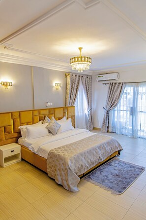 A bedroom with a large bed, a nightstand, a chandelier, and an air conditioning unit. - G&G Residency (Douala)