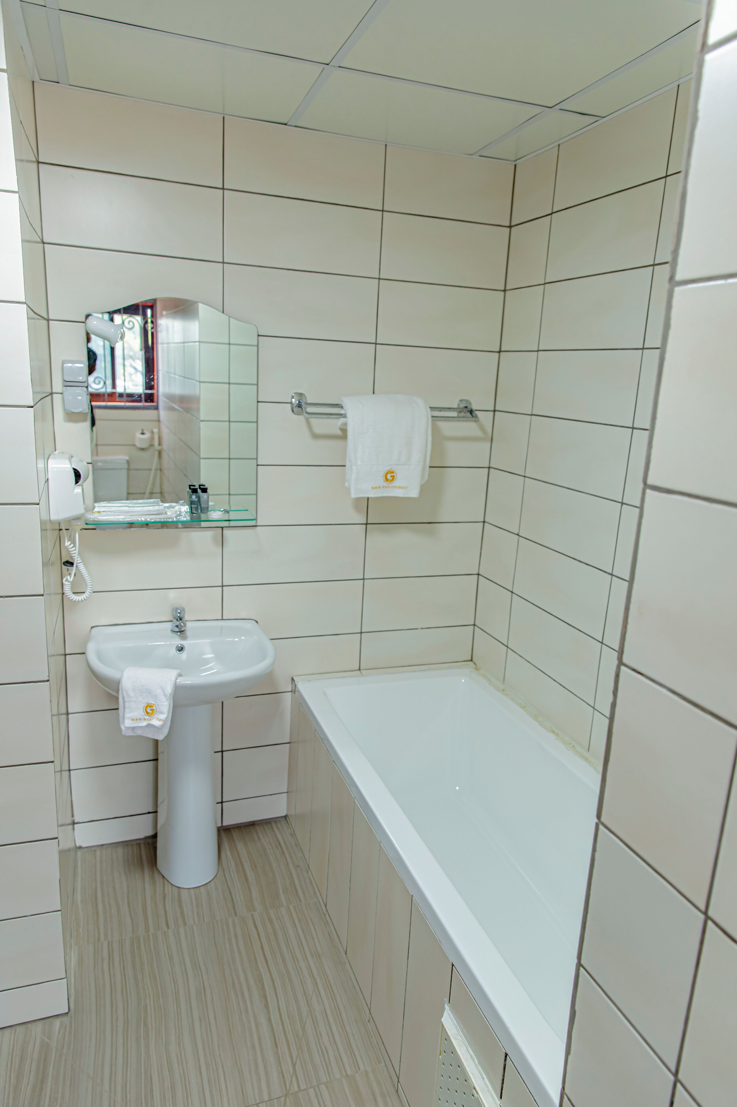 A bathroom with a white sink, a mirror, a towel rack, and a glass shelf with toiletries.