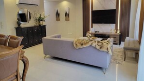 A modern living room with a sofa, a dining table, and a TV. - Upscale 3 Br Apartment For Family Or Friends Stay (Santo Domingo)