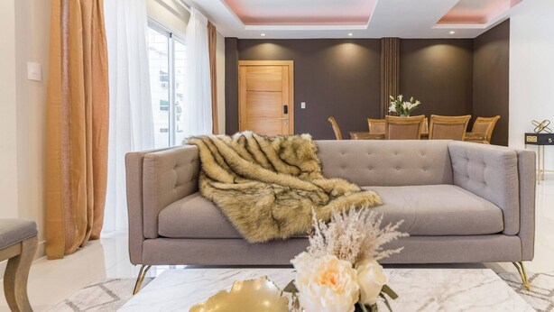 A modern living room with a grey sofa, a fur throw, and a vase with flowers on a marble table. - Upscale 3 Br Apartment For Family Or Friends Stay (Santo Domingo)