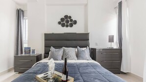 A modern bedroom with a large bed, a bedside table with a lamp, and a wall-mounted decorative piece. - Upscale 3 Br Apartment For Family Or Friends Stay (Santo Domingo)