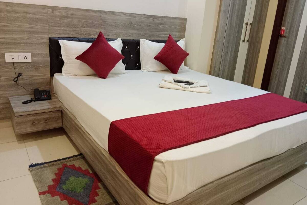 A neatly made bed with a red blanket, a bedside table with a phone, and a power outlet.