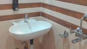 A bathroom with a white sink, a mirror, and a shower with multiple faucets. - L S Grand By GRB (Varanasi)