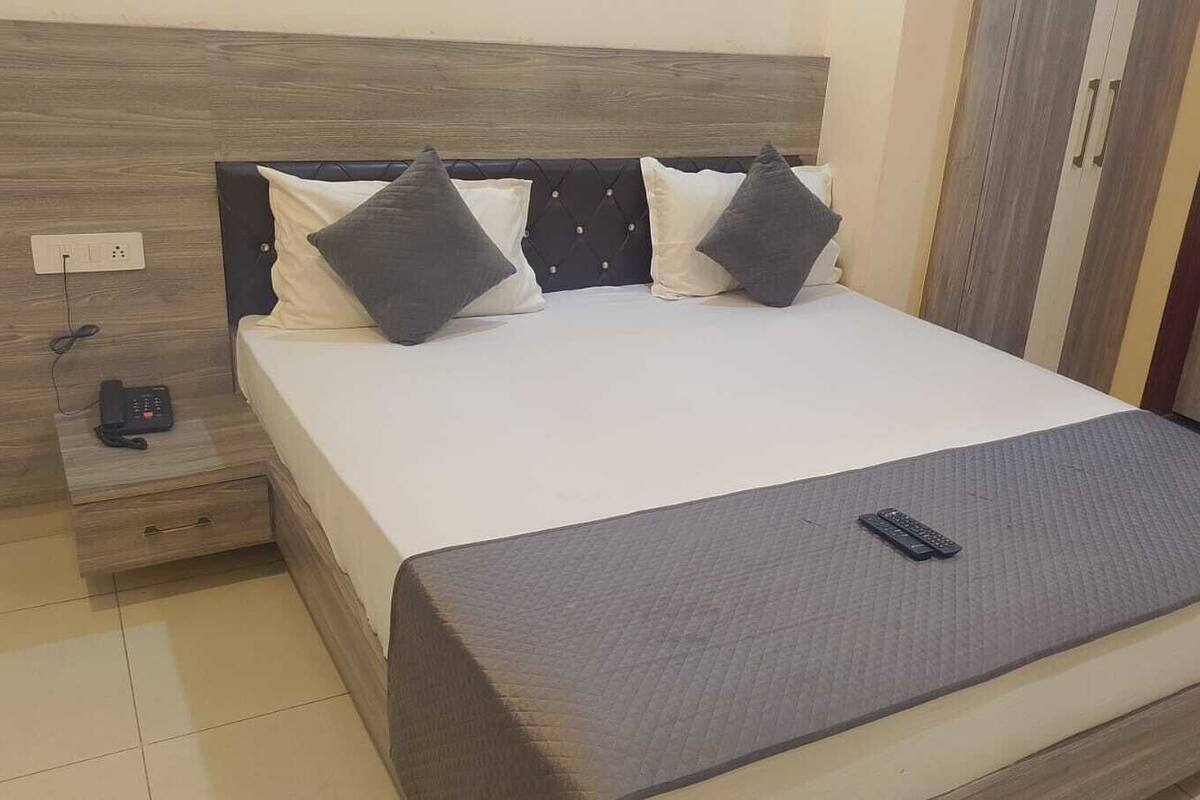 A neatly made bed with a grey blanket, two pillows, and a remote control on the bed.