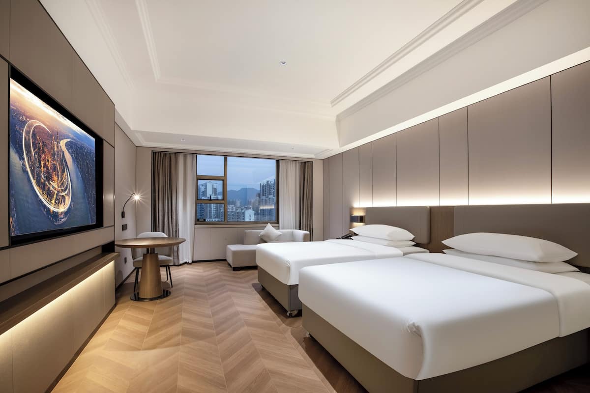 A hotel room with a large bed, a smaller bed, a seating area, a TV, and a city view.