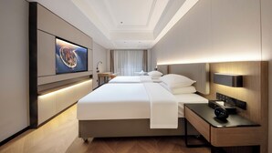 Ein modernes Hotelzimmer mit einem großen Bett, Nachttischen, einem Flachbildfernseher und einer Wandleuchte.