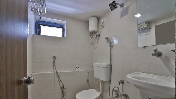 A bathroom with a toilet, a sink, a shower, and a window. - Hotel sudama palace (Ahmedabad)