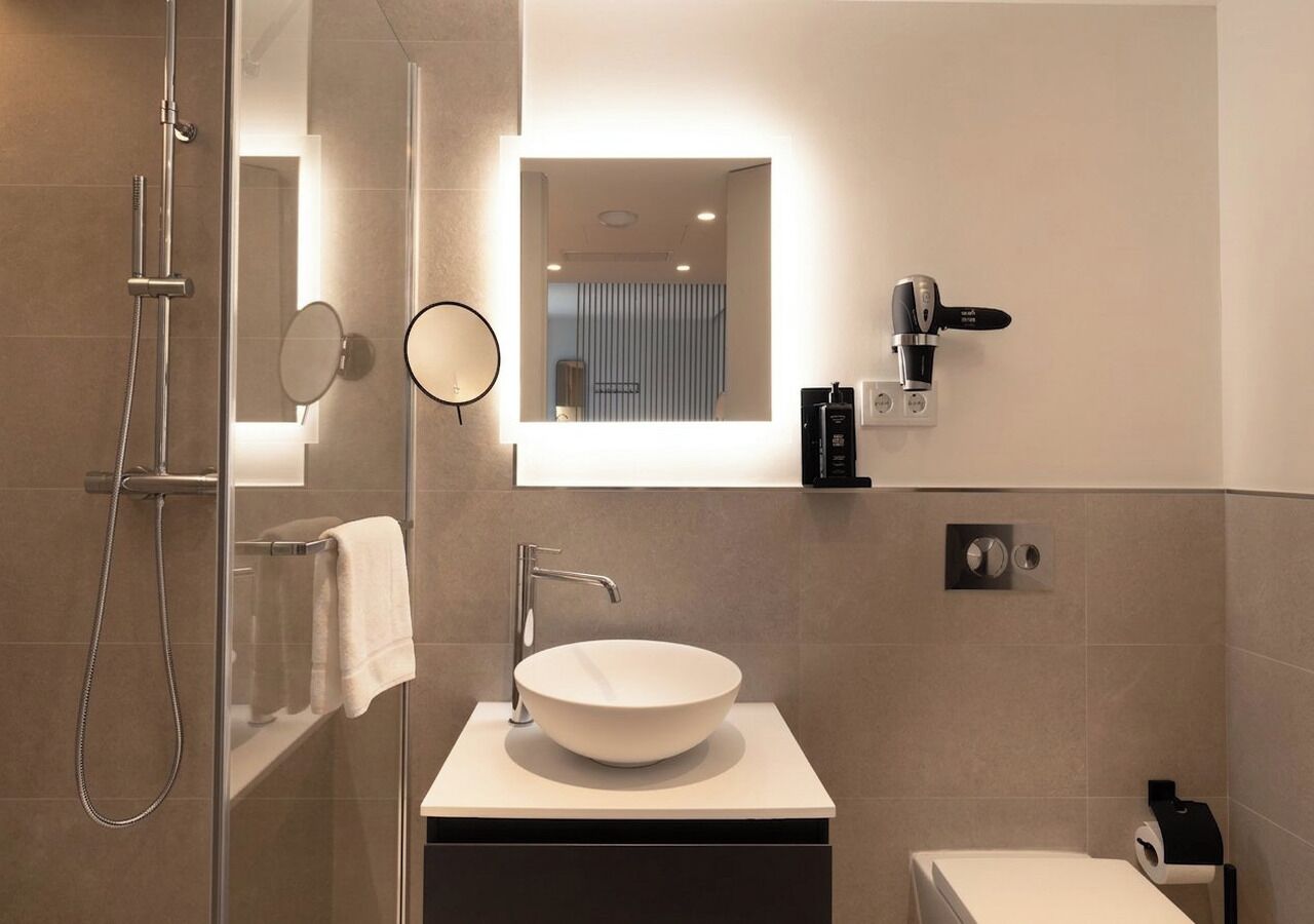 A modern bathroom with a glass-enclosed shower, a round mirror, a vessel sink, and a toilet.