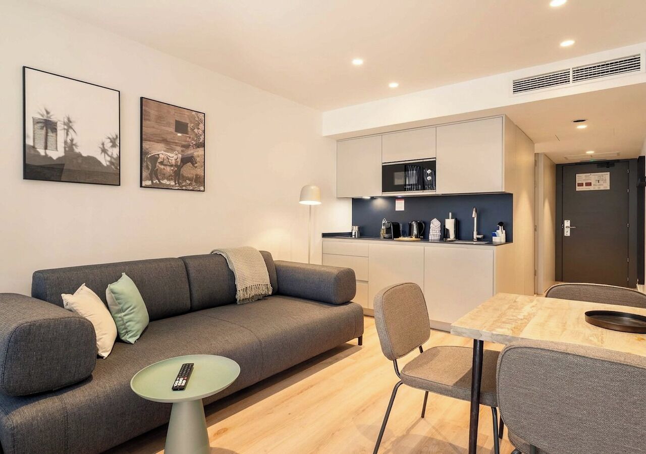 Ein modernes Wohnzimmer mit einer grauen Couch, einem kleinen runden Tisch und einem Essbereich mit Holztisch und Stühlen.