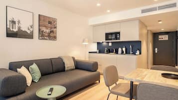 Ein modernes Wohnzimmer mit einer grauen Couch, einem kleinen runden Tisch und einem Essbereich mit Holztisch und Stühlen.