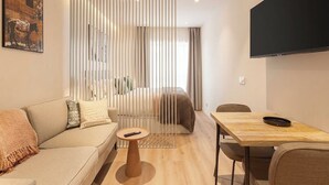 A modern living room with a sofa, a small round table, a dining table, and a TV mounted on the wall. - Limehome Madrid Calle Hurtado de Mendoza (Madrid)