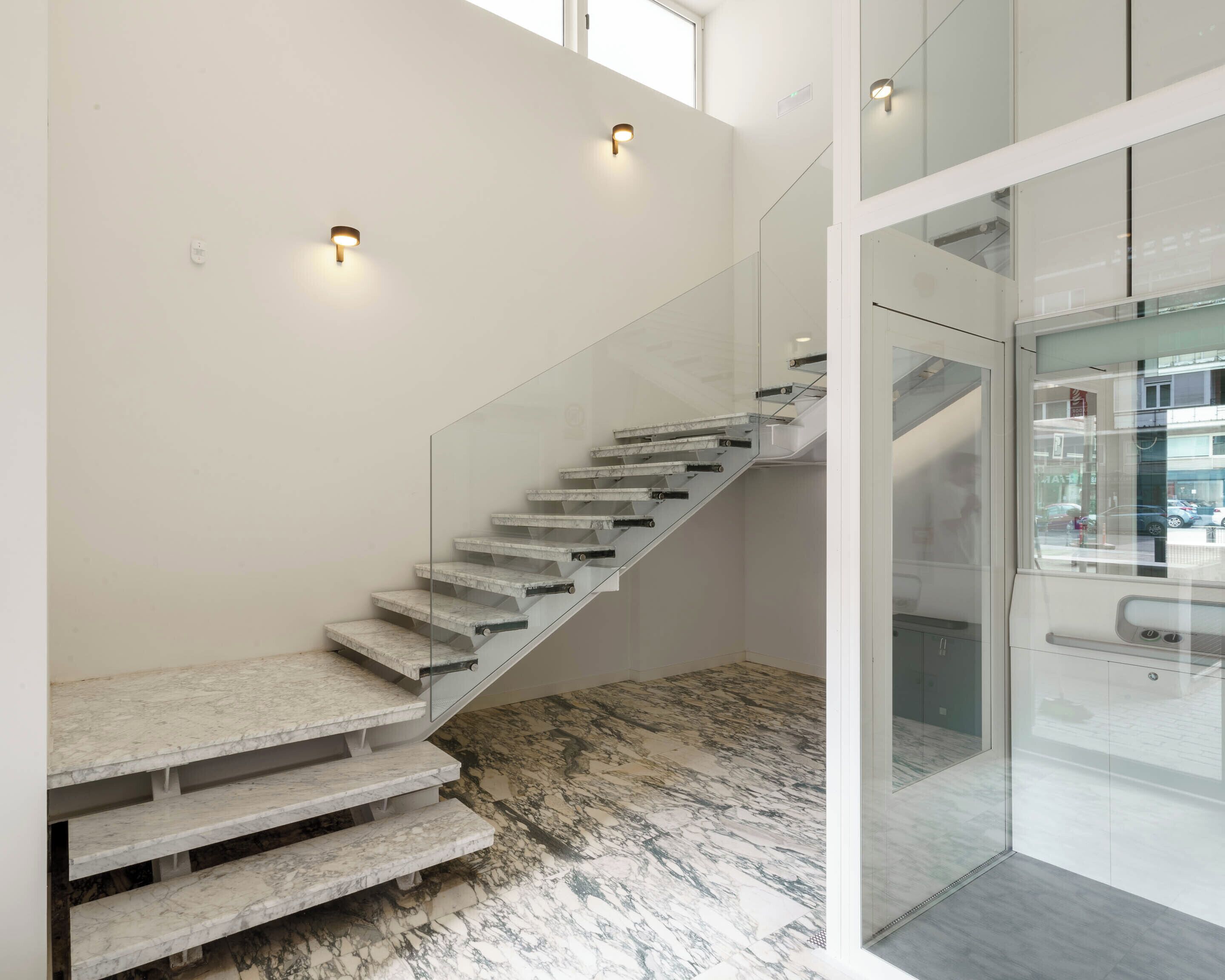 A modern staircase with glass railings and marble steps, leading to a glass door.