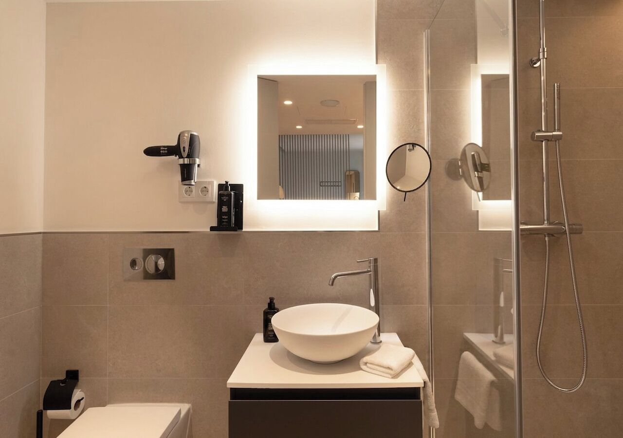 A modern bathroom with a large vessel sink, a handheld showerhead, a mirror, and a toilet.