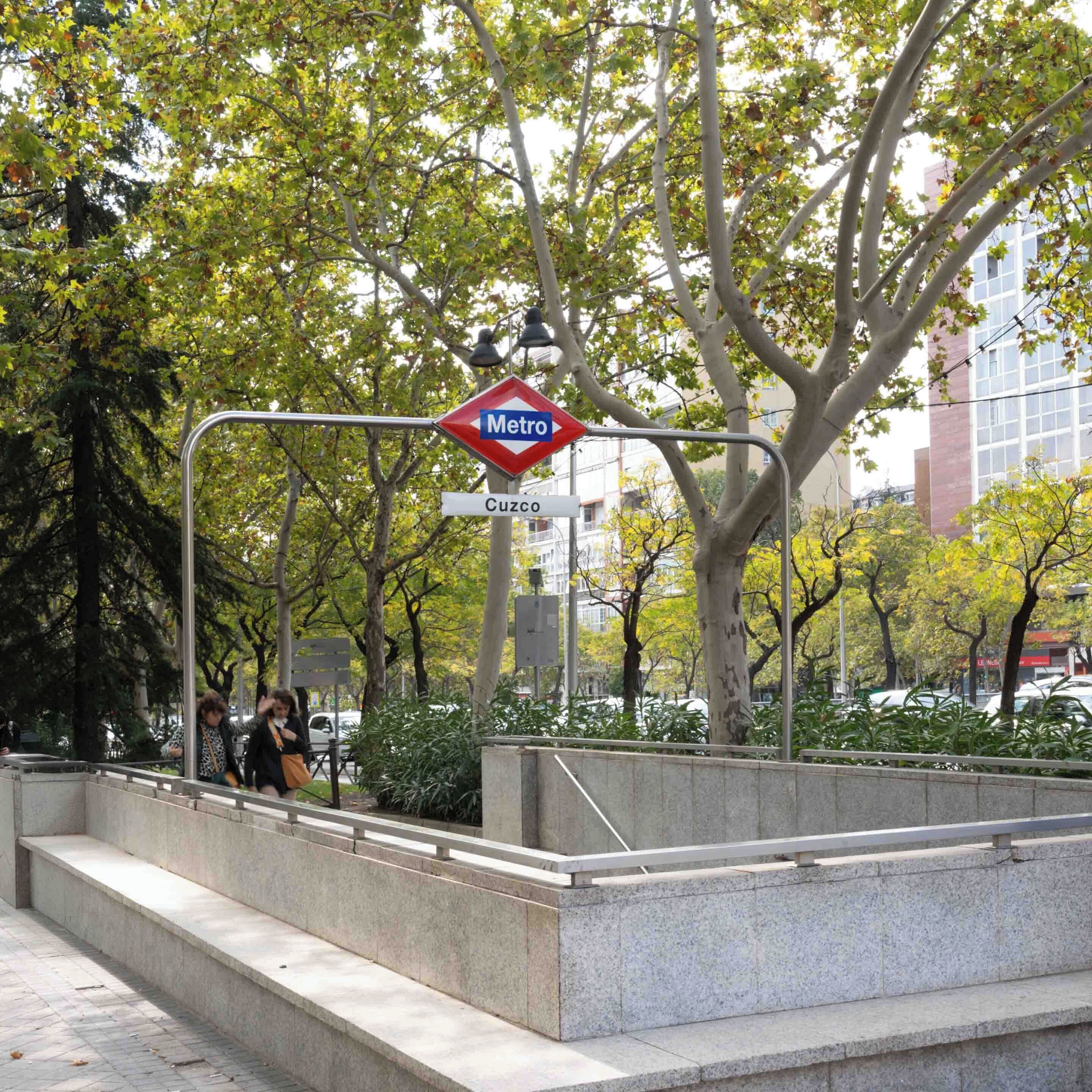 A metro station sign with a red diamond shape and the word "Metro" in white letters on a blue background. Below it, a white rectangular sign with "Cuzco" in black letters is visible.