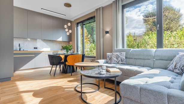 Ein modernes Wohnzimmer mit grauem Sofa, rundem Couchtisch und einem Essbereich mit Holztisch und Stühlen.