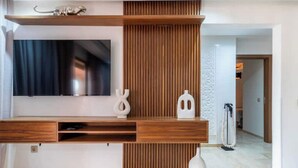 Una sala de estar moderna con un televisor de pantalla plana montado en una consola de madera, un panel decorativo en la pared y un pasillo que conduce a otra habitación.
