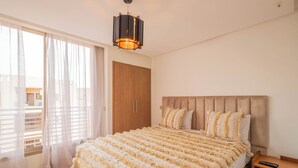 Un dormitorio con una cama grande, un armario de madera y un balcón con cortinas translúcidas.